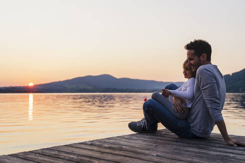 Smiling girl sitting on father's lap by lake, Mondsee, Austria - DIGF17412