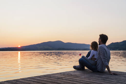 Vater und Tochter betrachten den Sonnenuntergang vom Steg aus, Mondsee, Österreich - DIGF17413