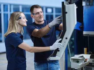 Technicians wearing protective eyewear discussing over CNC machine - CVF01769