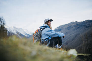 Mann mit Rucksack sitzt mit geschlossenen Augen auf einem Berg - OMIF00340