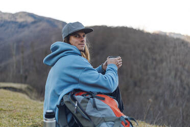 Hiker with backpack and coffee mug on mountain - OMIF00348