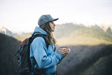 Nachdenklicher Mann mit Kaffeetasse und Rucksack im Urlaub - OMIF00349