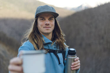 Smiling man with long hair and insulated drink container on mountain - OMIF00351