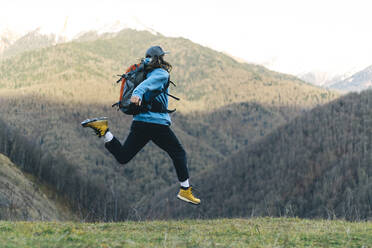 Rucksacktourist springt in Berglandschaft - OMIF00354