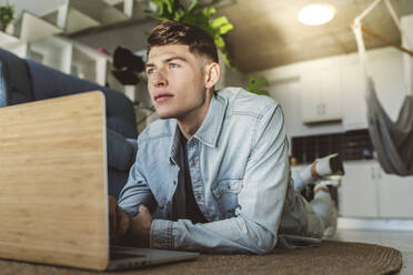 Young man lying on front with laptop in living room - JCCMF05029