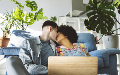 Young couple kissing on mouth with laptop in living room - JCCMF05031