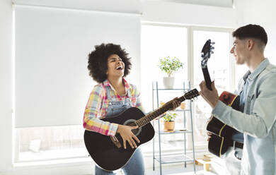 Fröhliches junges Paar, das zu Hause zusammen Gitarre spielt - JCCMF05034