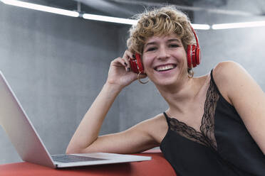 Cheerful businesswoman with laptop and wireless headphones - PNAF02728