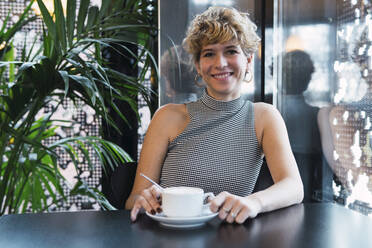 Smiling young woman with coffee cup sitting in cafe - PNAF02735