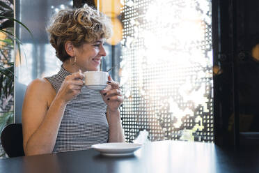 Lächelnde junge Frau mit Kaffeetasse in einem Cafe - PNAF02738