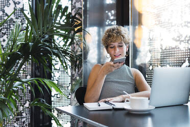 Freelancer sending voice message on smart phone at coffee shop - PNAF02743