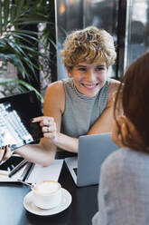 Smiling freelancer showing tablet PC to colleague in cafe - PNAF02749