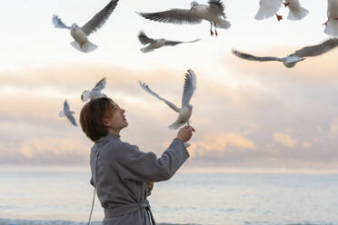 Young woman feeding seagulls at beach - SSGF00358