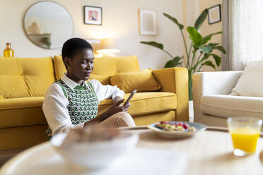 Frau mit Smartphone sitzt zu Hause auf dem Sofa - JCZF00880