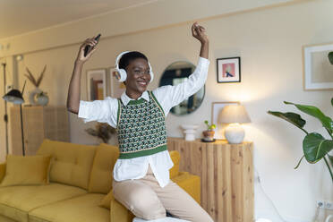 Cheerful woman dancing and listening through headphones at home - JCZF00891