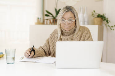 Geschäftsfrau mit Stift und Buch am Laptop auf dem Schreibtisch - JCZF00902