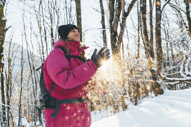 Smiling tourist dusting snow from hands in forest - OMIF00366