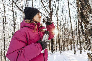 Tourist drinking water from insulated cup in snowy forest - OMIF00370