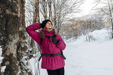 Nachdenklicher Tourist lehnt an einem Baum im Winterwald - OMIF00374