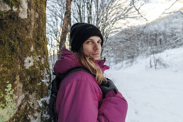 Tourist am Baumstamm stehend im Winterurlaub - OMIF00376