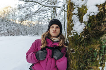 Tourist lehnt an Baumstamm im Winterwald - OMIF00378