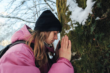 Man touching head on tree trunk in forest - OMIF00379