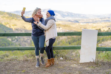 Friends taking selfie with smart phone leaning on railing - DLTSF02532