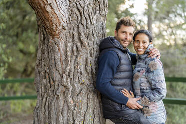 Man leaning on tree embracing woman at park - DLTSF02537