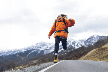 Unbekümmerter Wanderer, der im Winter über eine Bergstraße springt - OMIF00384