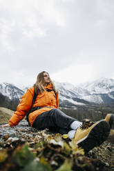 Mann in orangefarbener Jacke mit Blick auf die Aussicht im Winterurlaub - OMIF00389