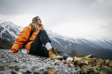 Wanderer mit Kaffeetasse nachdenklich auf Berg im Winter - OMIF00390