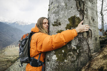 Tourist in orangefarbener Jacke, der einen Baumstamm umarmt - OMIF00394