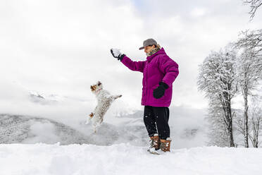 Hund springt auf Schneeball in der Hand eines Mannes zu - OMIF00411