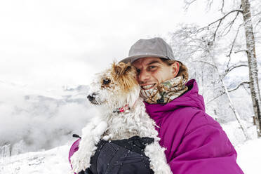 Lächelnder Mann macht Selfie mit Hund im Winterurlaub - OMIF00412