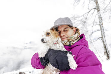 Man embracing Jack Russell terrier on winter vacation - OMIF00413