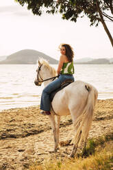 Young woman enjoying horse riding at waterfront - RSGF00797