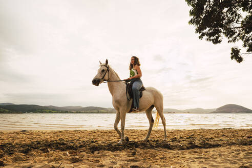 Junge Frau reitet auf einem Pferd am Wasser - RSGF00800