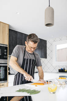 Mann mit Schürze schneidet Karotte in der Küche zu Hause - JRFF05226