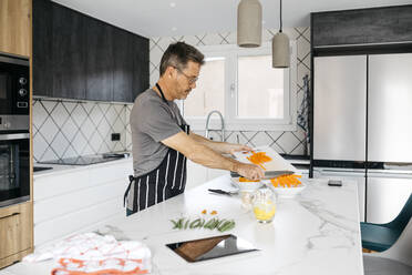 Man putting chopped carrots in bowl preparing food at home - JRFF05228