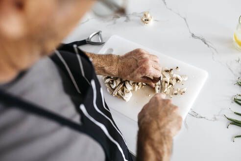 Man cutting mushrooms on cutting board at kitchen counter - JRFF05233