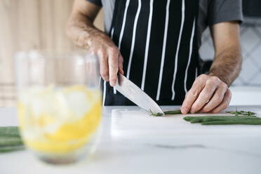 Mann schneidet grüne Bohnen mit Messer auf Schneidebrett in Küche - JRFF05236