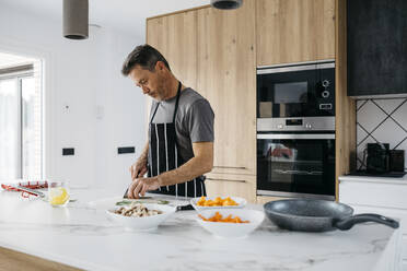 Man wearing apron cutting vegetables in kitchen at home - JRFF05237