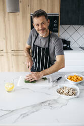 Lächelnder Mann hackt grüne Bohnen auf einem Schneidebrett in der Küche zu Hause - JRFF05239
