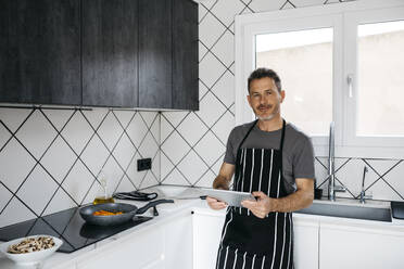Lächelnder Mann mit Tablet-PC, der sich zu Hause an die Küchentheke lehnt - JRFF05243