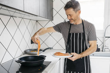 Lächelnder Mann beim Kochen von Fisch in der Küche zu Hause - JRFF05250