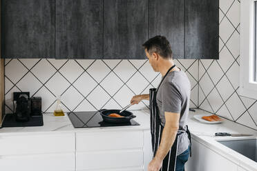 Man preparing fish in cooking pan on stove top at home - JRFF05253