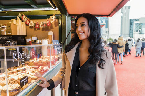 Smiling woman buying sweet food from shop in Christmas market - JRVF02387