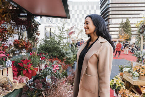 Smiling woman with overcoat at flower shop in Christmas market - JRVF02390