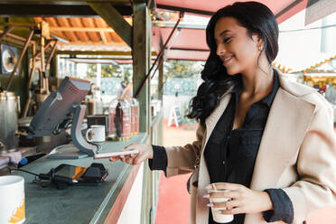 Frau bezahlt mit ihrem Smartphone an einem Imbisswagen auf dem Markt - JRVF02393