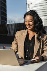 Glückliche Geschäftsfrau arbeitet am Laptop an einem sonnigen Tag - JRVF02398